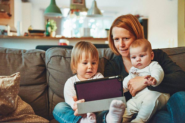Mother sitting on couch with toddler and baby on her lap